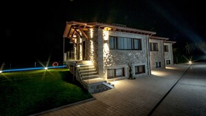 Ein Steinhaus mit überdachter Veranda, einem gepflasterten Auffahrtsweg und einem gut beleuchteten Eingang.