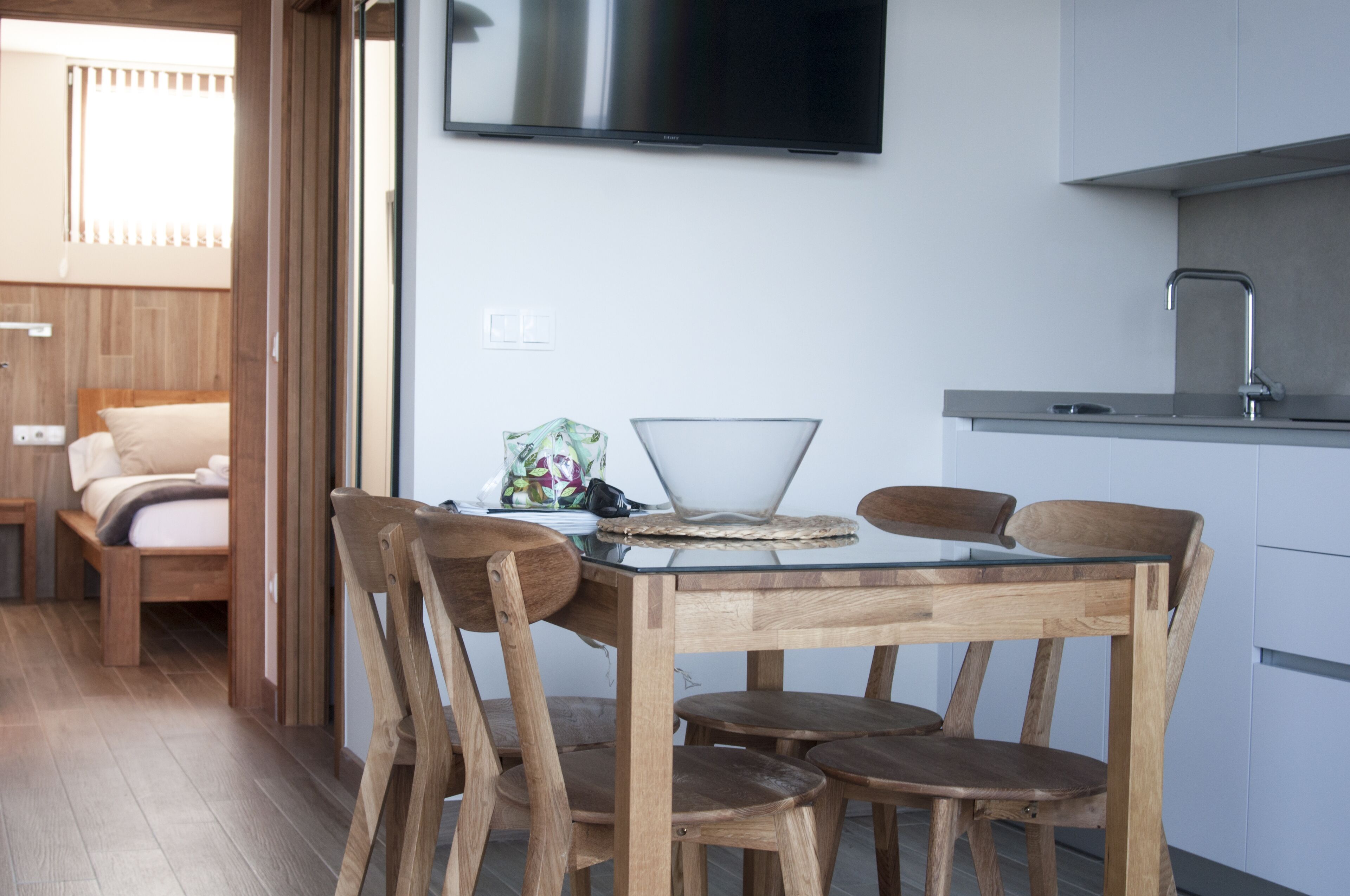 Une cuisine moderne équipée d’un téléviseur à écran plat, de chaises en bois, d’une table avec un plateau en verre et d’un évier encastré.