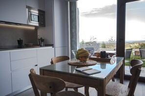 A modern kitchen with a glass dining table, wooden chairs, and a view of the outdoors.