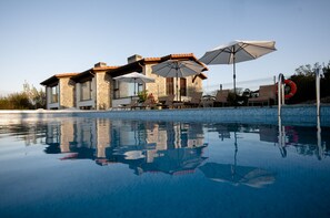 A modern house with a swimming pool, outdoor seating, and umbrellas.