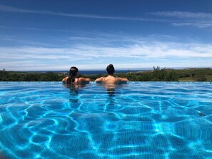 Una piscina infinita de color azul intenso con dos personas relajándose en el borde, con vistas a un paisaje pintoresco.