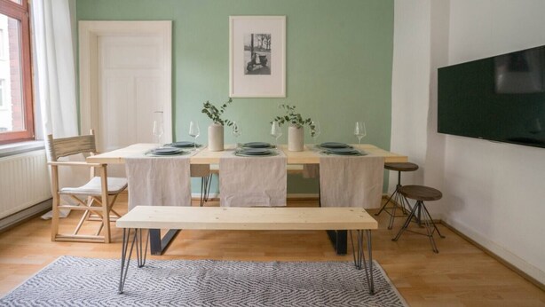 A dining area with a table set for four, a television on the wall, and a framed picture above the table. - pestahome - Private Apartment Linden / Hanover, pestahome - Stadtwohnung in Linden (Hanover)