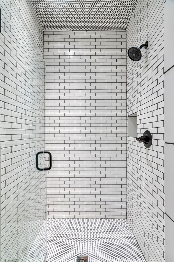 A modern shower with white tiled walls and floor, a black showerhead, and a small rectangular mirror. - Stunning farmhouse with Mountain View’s! (Sevierville)