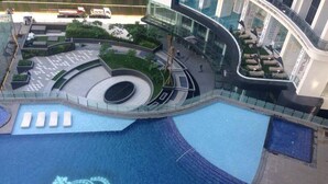 A modern building with a large pool featuring a crown design, surrounded by seating areas and greenery.