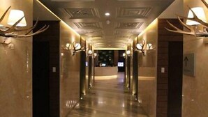A hotel corridor with marble floors, wall-mounted light fixtures, and decorative ceiling patterns.