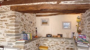 Una habitación acogedora con paredes de piedra, techo con vigas de madera, un taburete pequeño y una ventana con vistas.