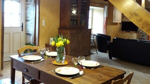 Un comedor con una mesa de madera dispuesta para cuatro personas, un jarrón con flores amarillas y una escalera al fondo.