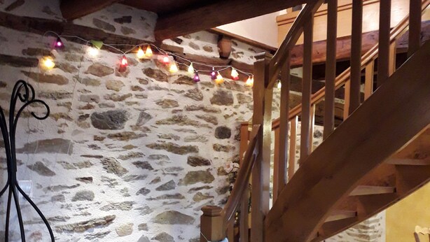 Una escalera de madera con un fondo de pared de piedra, una pequeña mesa de madera y una silla en una habitación con suelo de baldosas.