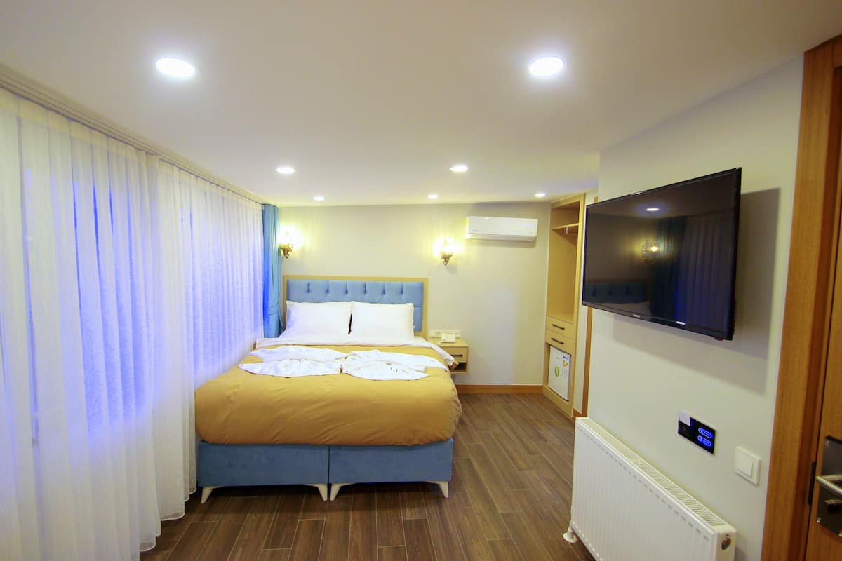 A hotel room with a bed, curtains, a television, and a thermostat.