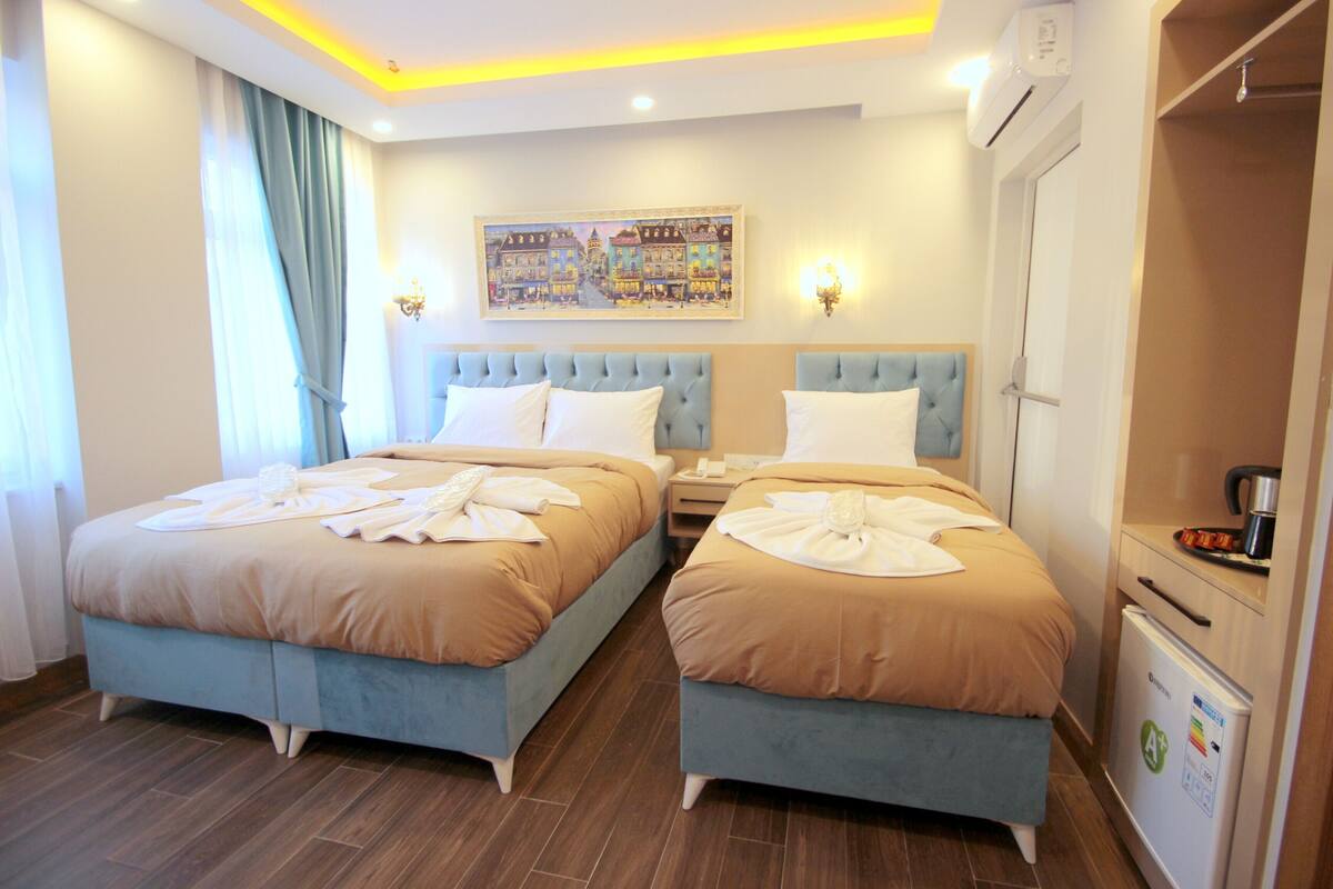 A hotel room with two beds, a painting on the wall, and a minibar.