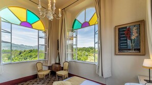 A hotel room with a bed, two chairs, a desk, and a large window with a view of greenery. - Splendid Liberty villa overlooking the lush green Tuscan valleys and mountains (Barga)