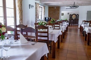Un restaurante con varias mesas dispuestas para comer, con sillas de madera y manteles blancos.