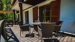 Una terraza de madera con muebles de mimbre y una mesa, con vistas a un jardín.