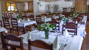 Un restaurante con varias mesas dispuestas para comer, cada una con sillas, manteles blancos y centros de mesa florales.