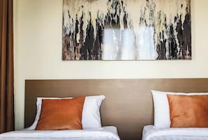 Habitación de hotel con dos camas, almohadas marrones y blancas, un cuadro abstracto grande en la pared y un adorno pequeño en la mesita de noche.