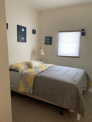 A bedroom with a bed, a nightstand, a lamp, a window with blinds, and wall decorations including a moon and anchor.