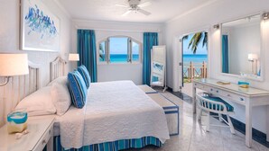 Ein Schlafzimmer mit Bett, Schreibtisch und Stuhl, ein großes Fenster mit Blick auf den Strand und einem Deckenventilator.