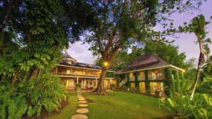 A large, two-story house with a well-maintained garden, a stone pathway, and a staircase leading to the upper floor.