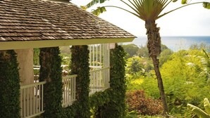 A house with a tiled roof and a balcony with white railings, surrounded by lush greenery and a view of the ocean. - 17th Century Sugar Mill Near Beach - Mullins Mill (Mullins)