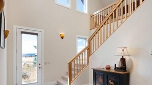 Un hall d’entrée spacieux avec un escalier en bois, une porte donnant sur l’extérieur et un buffet en bois sombre sur lequel est posée une lampe.