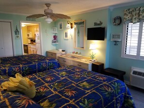 A bedroom with two beds, a ceiling fan, a dresser, a vanity, a mirror, and a window with blinds. - Dave's Vacation Rentals - Palms resort (Myrtle Beach)