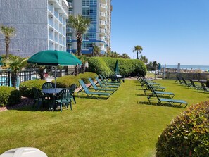 A poolside area with lounge chairs, a table, and umbrellas. - Dave's Vacation Rentals - Palms resort (Myrtle Beach)