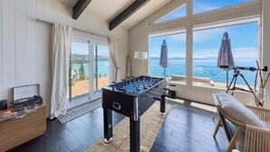 Una habitación con mesa de fútbol de mesa, sofá y telescopio cerca de amplios ventanales con vistas al mar.