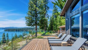A wooden deck with lounge chairs overlooking a lake and forest.