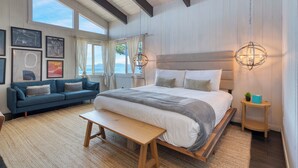 A bedroom with a large bed, a bench, a sofa, and a nightstand with a plant.