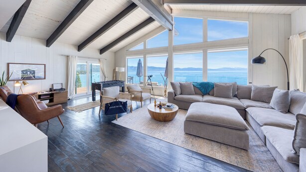 A spacious living room with a high ceiling, large windows, and a view of the ocean.