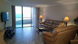 A spacious living room with a leather sofa, a coffee table, and a flat-screen TV. There is a balcony with a view of the sea. - Beautiful Marco Island Renovated Condo, 2 Br 2 Ba, 1704 T4,  Beach & Ocean Views (Marco Island)