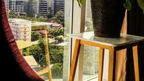 A window with a view of a cityscape, a potted plant on a small table, and a red chair in the foreground. - A SPACIOUS AND LUXURIOUS APARTMENT W/ 3 BEDROOM (Cebu City)