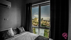 A bedroom with a large window, a bed with pillows, and a view of a cityscape. - A SPACIOUS AND LUXURIOUS APARTMENT W/ 3 BEDROOM (Cebu City)