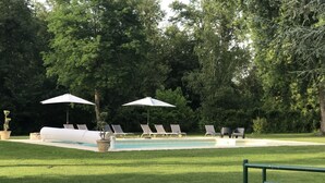 A pool area with lounge chairs and umbrellas, surrounded by trees.