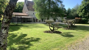 A courtyard with a stone building, a covered seating area, and neatly trimmed trees.