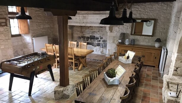 A rustic dining area with a long wooden table, chairs, and a foosball table.
