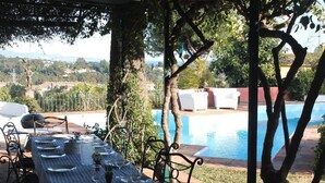 Un área de comedor al aire libre con una mesa preparada para cuatro, con vistas a una piscina y un paisaje campestre.