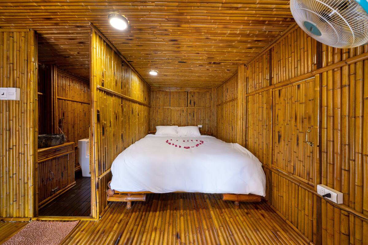 A room with a bed, a fan, and bamboo walls.