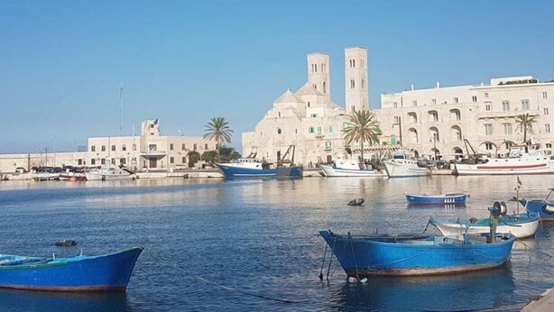 A marina with several boats docked, a large building with two towers, and a clear blue sky. - B&b Oltre l'Arco (Molfetta)
