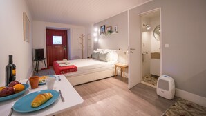 A compact bedroom with a bed, bedside table, and a small sitting area. - Rose 7 Studio Apartment (Lisboa)