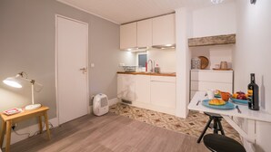 A compact kitchen with white cabinets, a dining table with a chair, and a small side table with a lamp. - Rose 7 Studio Apartment (Lisboa)