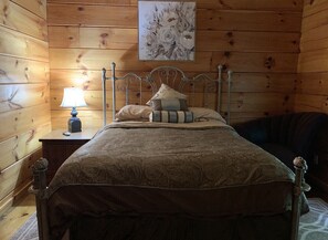 Una stanza con rivestimento in legno, un letto con struttura in metallo, un comodino con una lampada e un quadro floreale appeso alla parete.