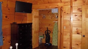 A wooden cabin interior with a television mounted on the wall, a dresser, and a vacuum cleaner in the room.