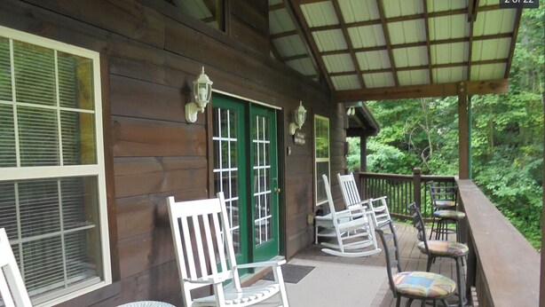 A wooden porch with rocking chairs and a small table, a green door, and a covered area with a railing.