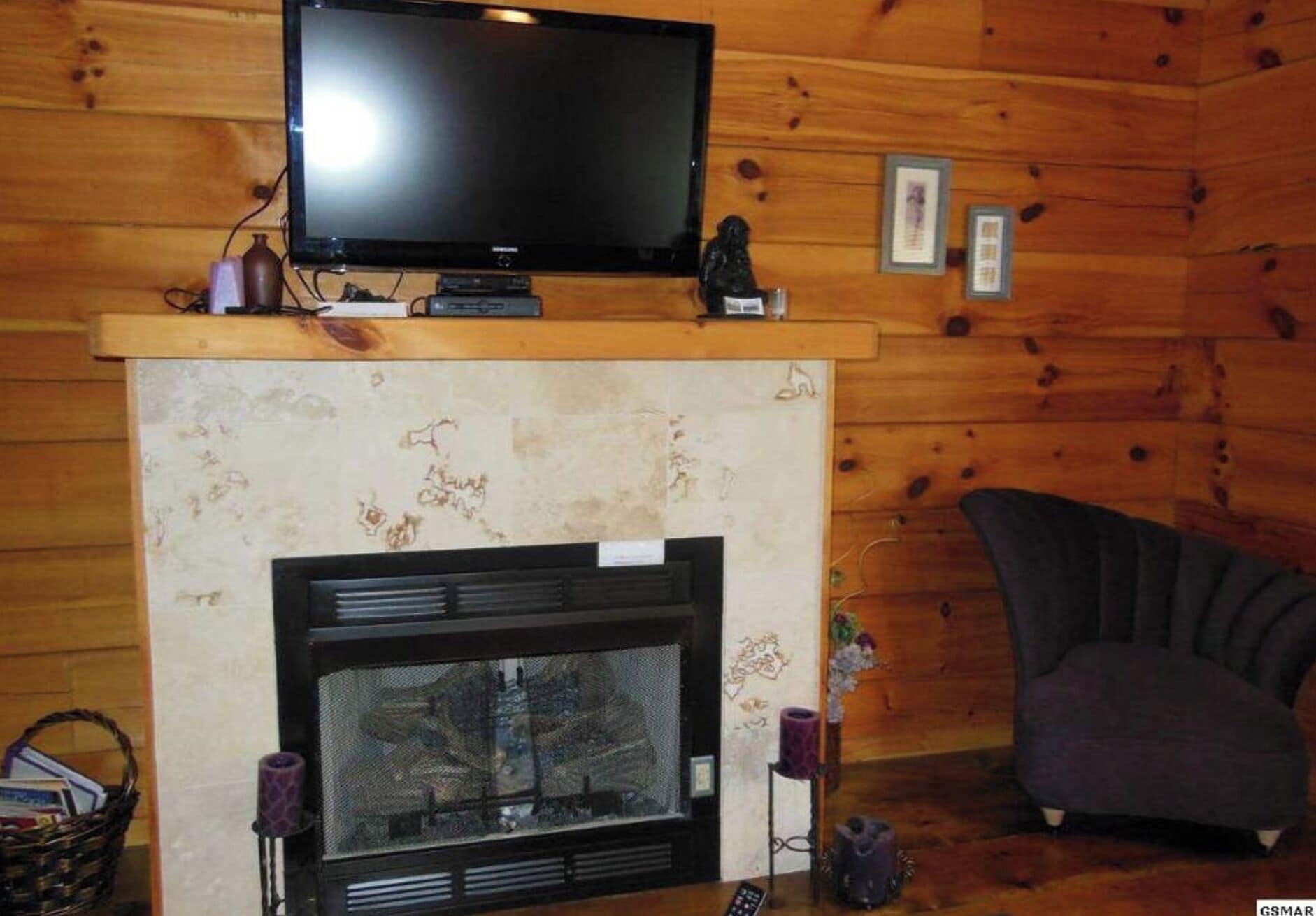 Interior acogedor de una cabaña con chimenea, un televisor montado encima y un sillón cómodo.