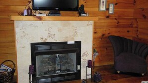 A cozy cabin interior with a fireplace, a television mounted above it, and a comfortable armchair.