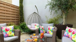 A wicker outdoor seating area with cushioned chairs and a hanging chair, a glass table with breakfast items, and a wooden fence in the background. - Luxurious Vacation Rental 10 mins walk from Epernay town centre (Épernay)