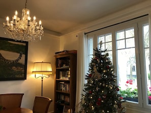 Ett mysigt vardagsrum med en kristallkrona, en bokhylla, en julgran och en matplats.