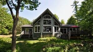 A two-story house with a prominent gable roof, a front porch with steps, and a deck on the right side. - Woods Bay Lookout, Georgian Bay (The Archipelago)