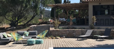 A poolside area with outdoor furniture, a pergola, and a stone wall.